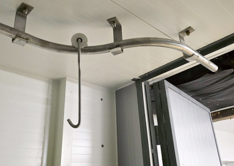 
Dzesētavas griestos ir iestrādāti speciāli jaudīgi metāla stiprinājumi, pie kuriem ir pieskrūvētas apmēram septiņu centimetru diametra nerūsējošā tērauda caurules. Papildus ir izgatavoti jaudīgi āķi ar tērauda skritulīšiem, kas brīvi un bez aiztures ripo pa šīm caurulēm.
